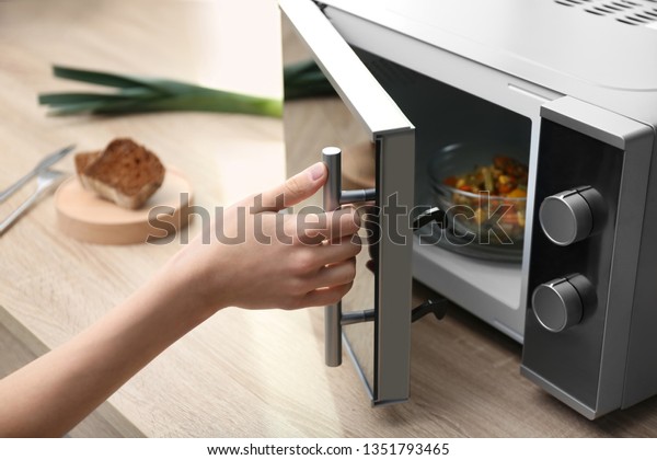 Young\
woman using microwave oven on table in\
kitchen