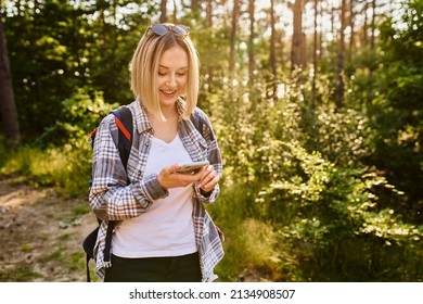 Young Woman Using Mobile Phone While Walking In The Woods During Summer Hike