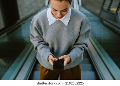 Young Woman Using Mobile Phone While Going Up The Escalator Outdoors