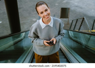 Young Woman Using Mobile Phone While Going Up The Escalator Outdoors