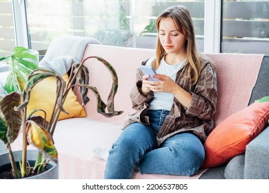 Young Woman Using Mobile Phone For Searching Info About Houseplants Disorders, It's Identification And Treatment For Dried, Sunburn Leaf Of Potted Plant Calathea. Houseplants Diseases. Home Gardening.