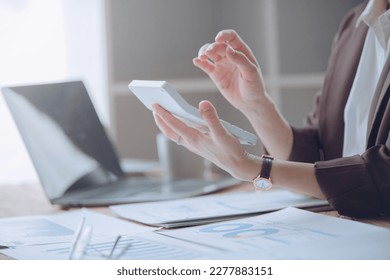 Young woman using mobile phone, laptop and calculator working on wooden table in office. Business and finance concept.