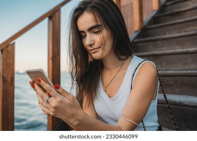 Young woman using mobile phone sitting on brown wooden staircase - Powered by Shutterstock