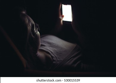 Young Woman Using Mobile Phone In Dark Room At Home