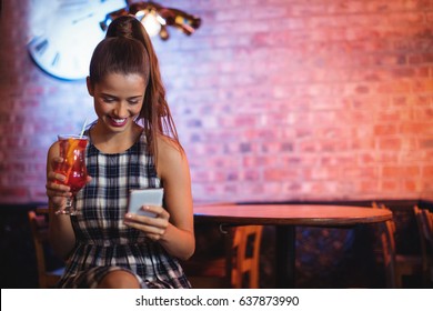 Young woman using mobile phone while having cocktail drink in pub - Powered by Shutterstock