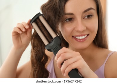 Young Woman Using Modern Curling Iron Indoors