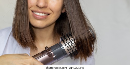 young woman using a modern rotative hair brush to style her hair.smiling girl, close up.hair dryer and volumizer. Thermal and ceramic coating of dryer.hair styler rotating brush with attachments