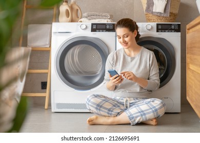 Young Woman Is Using Phone While Doing Laundry At Home.