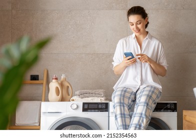 Young woman is using phone while doing laundry at home. - Powered by Shutterstock