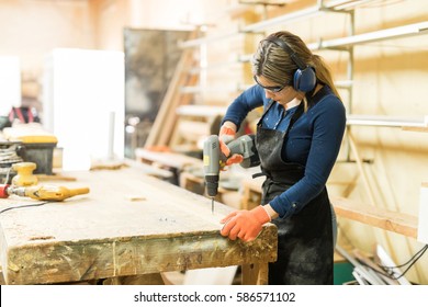 Young Woman Using A Screwdriver On A Piece Of Wood While Working In A Woodshop