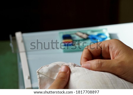 A young woman is using a sewing needle to fix her clothes to be able to perform well as before, in order to reduce her daily expenses.
