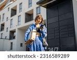 Young woman using smart phone while standing with a parcel delivered with post office machine with automatic lockers. New technologies in delivery service, self picking