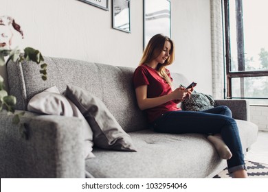 Young woman using smart phone while relaxing on couch at living room