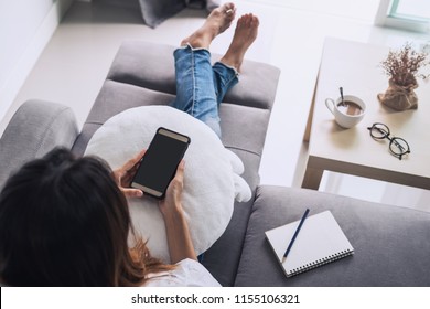 Young Woman Using Smart Phone And Relax On Sofa In Living Room At Cozy Home