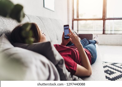 Young woman using smart phone while lying on the couch at home