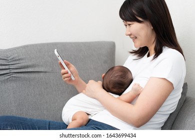 Young woman using smart phone with baby
