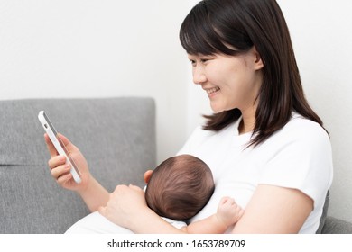 Young woman using smart phone with baby
