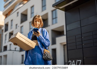 Young woman using smart phone while standing with a parcel delivered with post office machine with automatic lockers. New technologies in delivery service, self picking