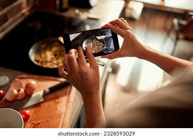 Young woman using a smart phone to take a picture of a meal she is cooking - Powered by Shutterstock