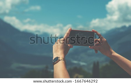 Young woman using smart phone camera for making picture of Swiss Alps. Female traveler blogger taking photos on mobile phone during summer journey vacations.