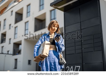 Young woman using smart phone while standing with a parcel delivered with post office machine with automatic lockers. New technologies in delivery service, self picking