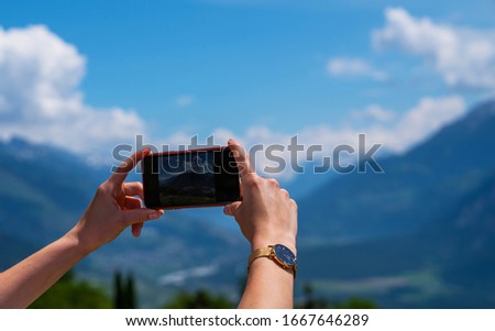 Young woman using smartphone camera for making picture of Swiss Alps. Female traveler blogger taking photos on mobile phone during summer journey vacations.