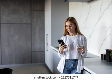 Young woman using smartphone leaning at kitchen table with coffee mug and organizer in a modern home. Smiling woman reading phone message. Brunette happy girl typing a text message - Powered by Shutterstock