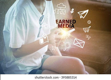 young woman using smartphone and pointing at  EARNED MEDIA  text on virtual screen. soft light with vintage filter. Internet concept.