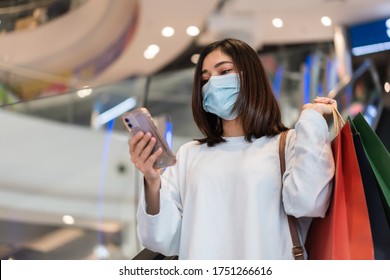 Young Woman Using Smartphone At Shopping Mall And Her Wearing Medical Mask For Prevention From Coronavirus (Covid-19) Pandemic. New Normal Concepts