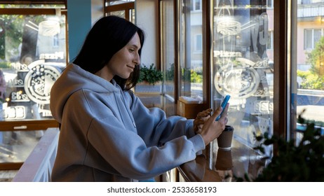 Young woman using smartphone while enjoying coffee in a cozy café during the daytime - Powered by Shutterstock