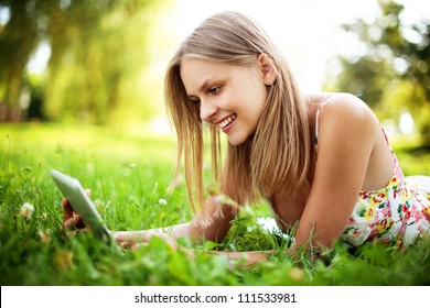 Young woman using tablet outdoor laying on grass, smiling. - Powered by Shutterstock