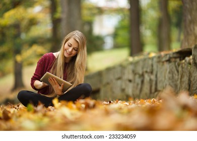 Young Woman Using Tablet Outdoor Sitting On Grass And Smiling. Girl Using Digital Tablet Pc In The Park. Student Using Tablet After School.