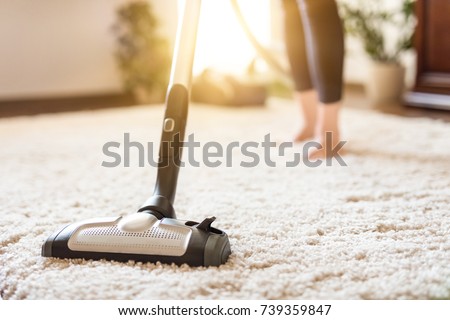 Young woman using a vacuum cleaner while cleaning carpet in the house.