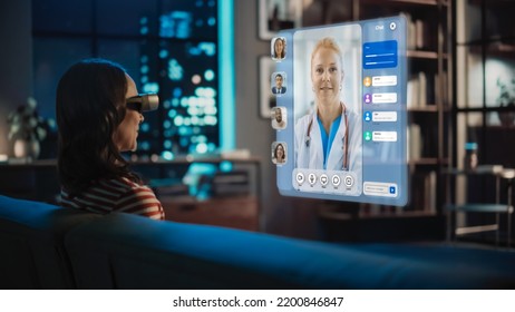 Young Woman Using Virtual Reality Headset At Home, Sitting On Couch In Living Room, Making Gestures To Answer AR Video Call With Family Doctor. Medical Health Online Examination And Doctor Visit.