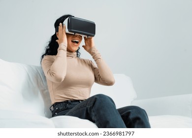 Young woman using virtual reality VR goggle at home for crucial online shopping experience. The virtual reality VR innovation optimized for female digital entertainment lifestyle. - Powered by Shutterstock