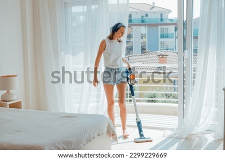 Young woman vacuuming the floor in bright cozy room with cordless vacuum cleaner. High quality photo