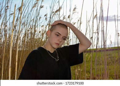 Young Woman With Very Short Hair In Front Of Tall Grass In Nature, Hand On The Top Of The Head