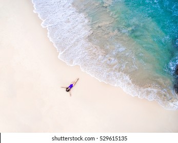 Young woman in a violet bikini lying on the back on the sand near the waves of blue sea. Top view. Surin beach, Andaman Sea, Phuket, Thailand. Aerial Shooting.