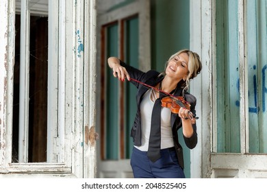 young woman violinist, in an old country house, in nature, in a black suit with a tie, plays the violin