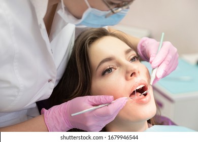 Young Woman Visit Dentistry Clinic For Professional Teeth Treatment. Woman Dentist Bend Over Patient. Doctor Holding Instrument Tool For Oral Examination. Professional Toothache Cure. Stomatology