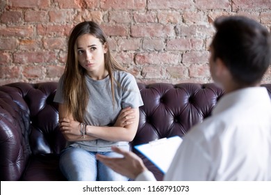 Young Woman Visiting Psychologist Counselor. Upset Teenage Girl Looks At Doctor With Distrust, Disagree, No Desire To Talk. Teenage Problems, Depression, Misunderstanding, Quarrel With Parents, Trauma