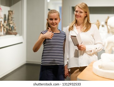 Young Woman Visitor With Daughter With Guide Book Looking At Exhibition In Museum Of Art