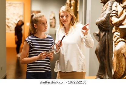 Young Woman Visitor With Daughter With Guide Book Looking At Exhibition In Museum Of Ancient Sculpture