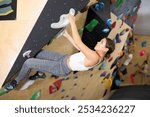 Young woman visitor to fitness club clambs obstacle course on wall for amateur climbers, side view. Active recreation, hobbies, recreation for active and sporty people