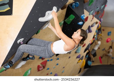 Young woman visitor to fitness club clambs obstacle course on wall for amateur climbers, side view. Active recreation, hobbies, recreation for active and sporty people - Powered by Shutterstock