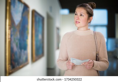 Young Woman Visitor With Guide Book Looking At Exposition In Art Museum