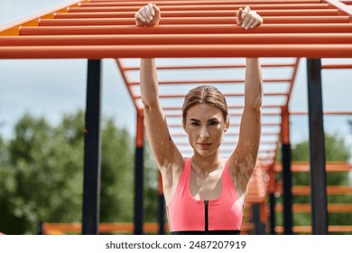 A young woman with vitiligo in pink sportswear hangs from a monkey bar at an outdoor gym. - Powered by Shutterstock