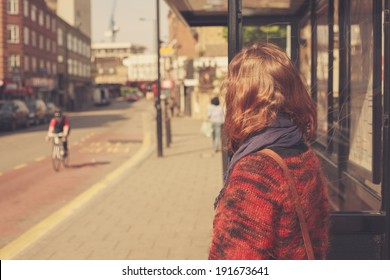 A young woman is waiting at the bus stop on a sunny day