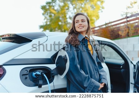 Young woman waiting while her electric car charging in home charging station, sustainable and economic transportation concept.