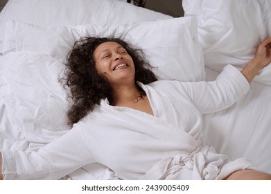 Young woman waking up in her white bed in the morning. Cheerful young woman in white waffle bathrobe, expressing happy positive emotions, laughing, smiling, lying on bed, enjoying a happy weekend - Powered by Shutterstock